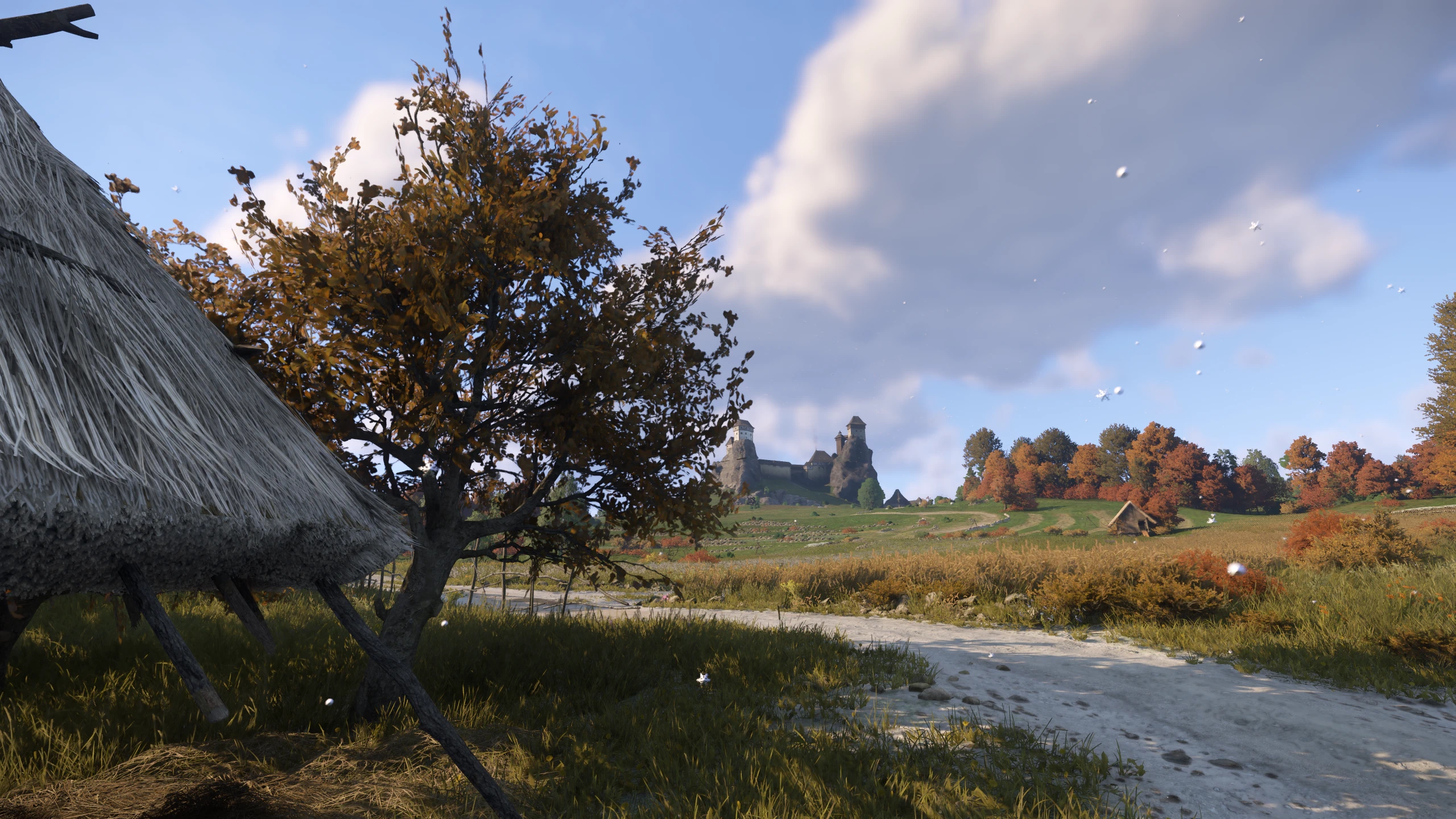 Light snow drifts over an autumn-colored Bohemian village and the distant towers of Trosky.