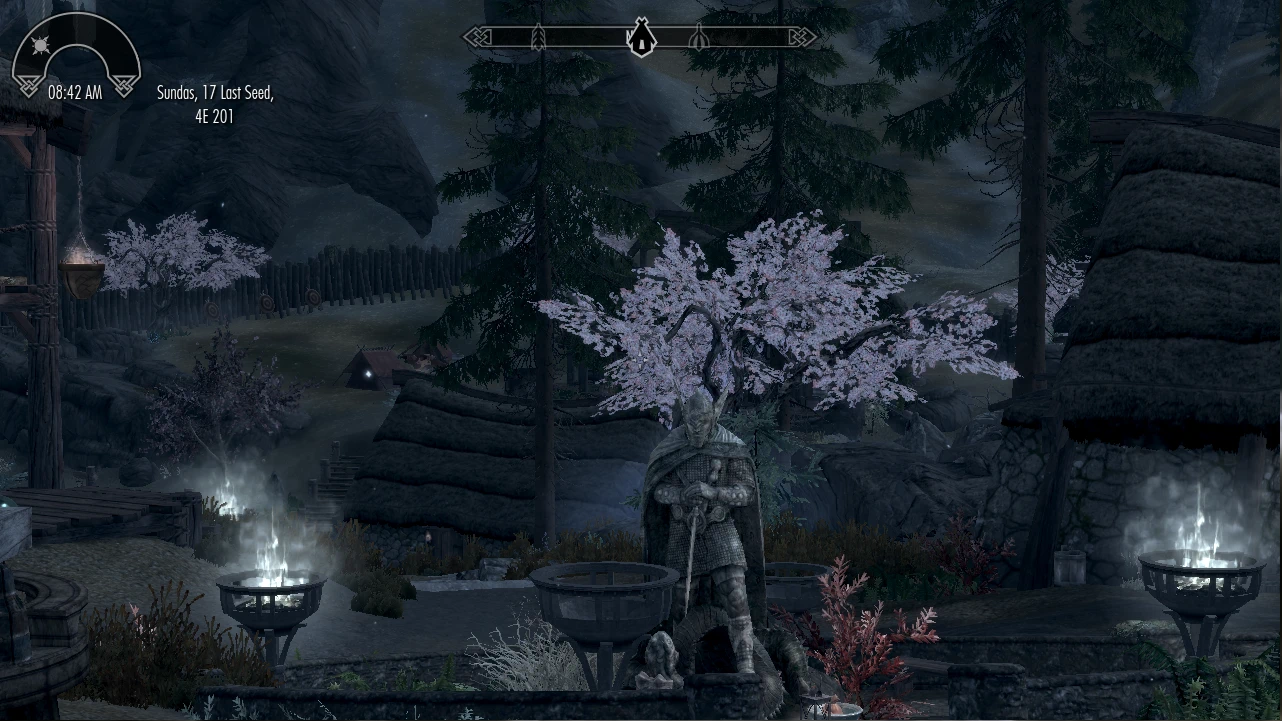 Wooden buildings and a central statue stand among trees in a dark wooded Skyrim settlement.