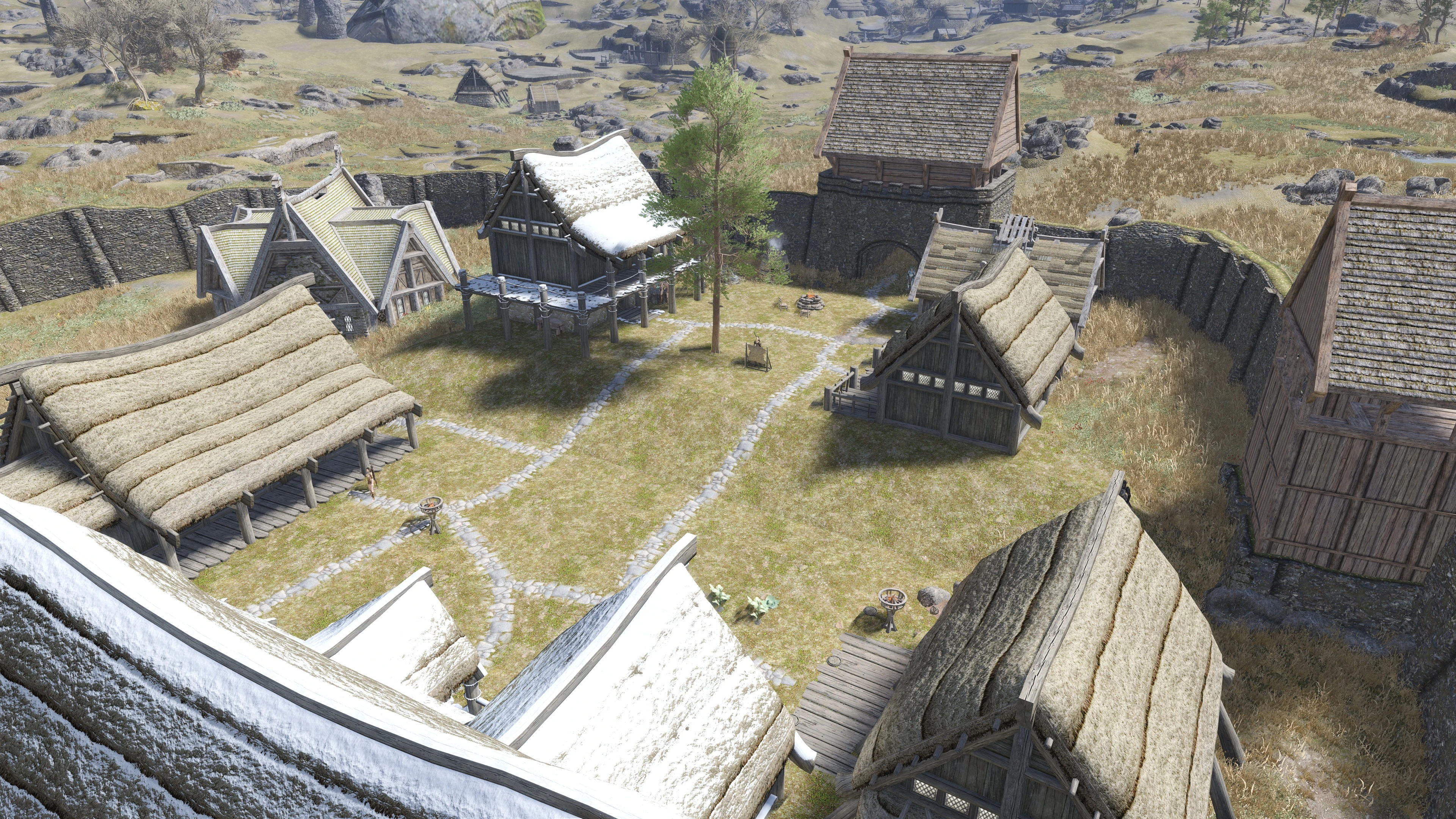 An elevated view of a player-built Skyrim settlement with houses, stone paths, walls and gate towers.