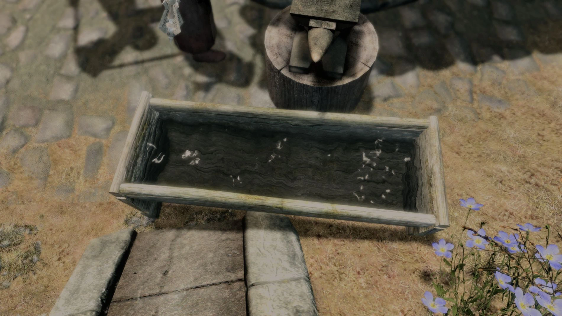 Reflective water fills a wooden forge quench trough beside a blacksmith’s anvil in Skyrim.