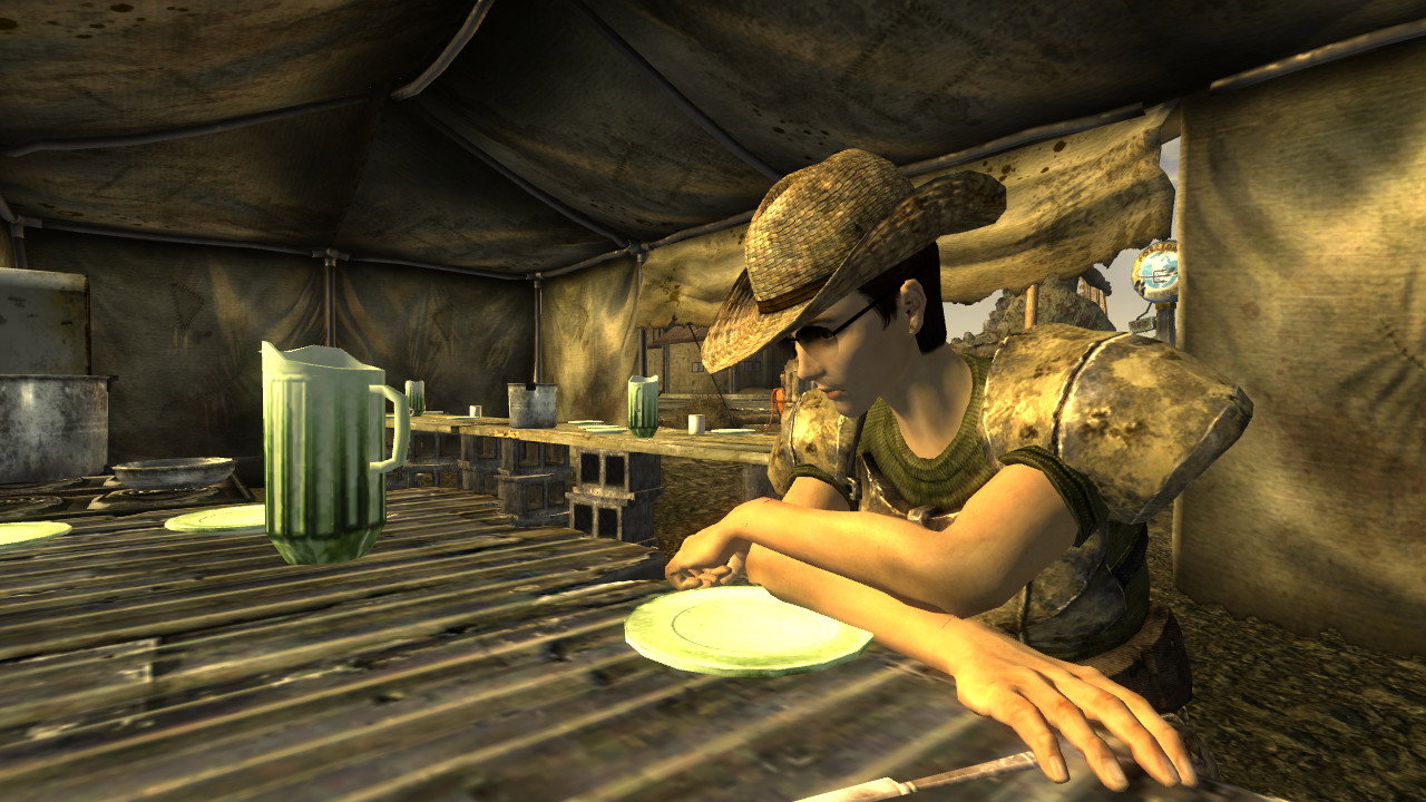 Rourke sits at a table inside a canvas tent, wearing a hat, sunglasses and shoulder armor.