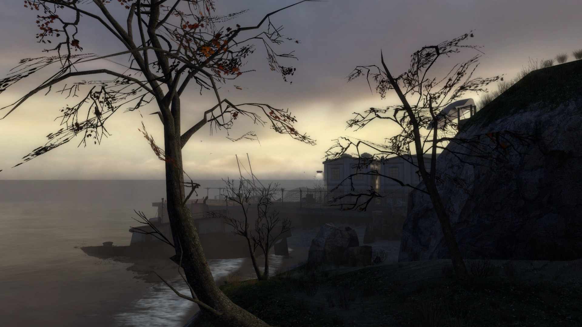 Bare trees frame a waterfront building and rocky shoreline on MINERVA’s island at dusk.